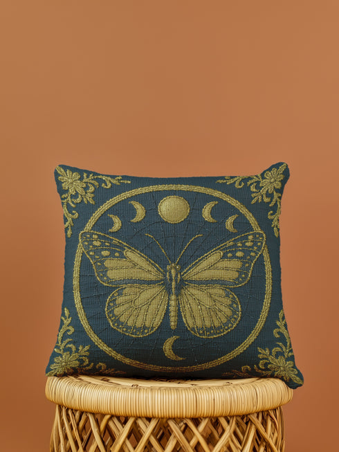 A square woven tapestry pillow in charcoal grey and metallic gold thread, embodying a premium, artisan feel. The central design features an intricate butterfly, a nod to entomology decor, encircled by a celestial moon phase motif. This combination of mystical and dark botanical elements makes it ideal for Whimsigoth, Gothic, and Dark Academia aesthetics. Ornate Victorian flourishes in the corners complete this luxurious, double-sided piece of functional art.
